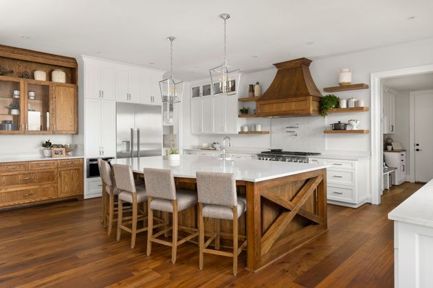 Modern kitchen with wood floors, central island, stainless steel appliances, and a large range hood