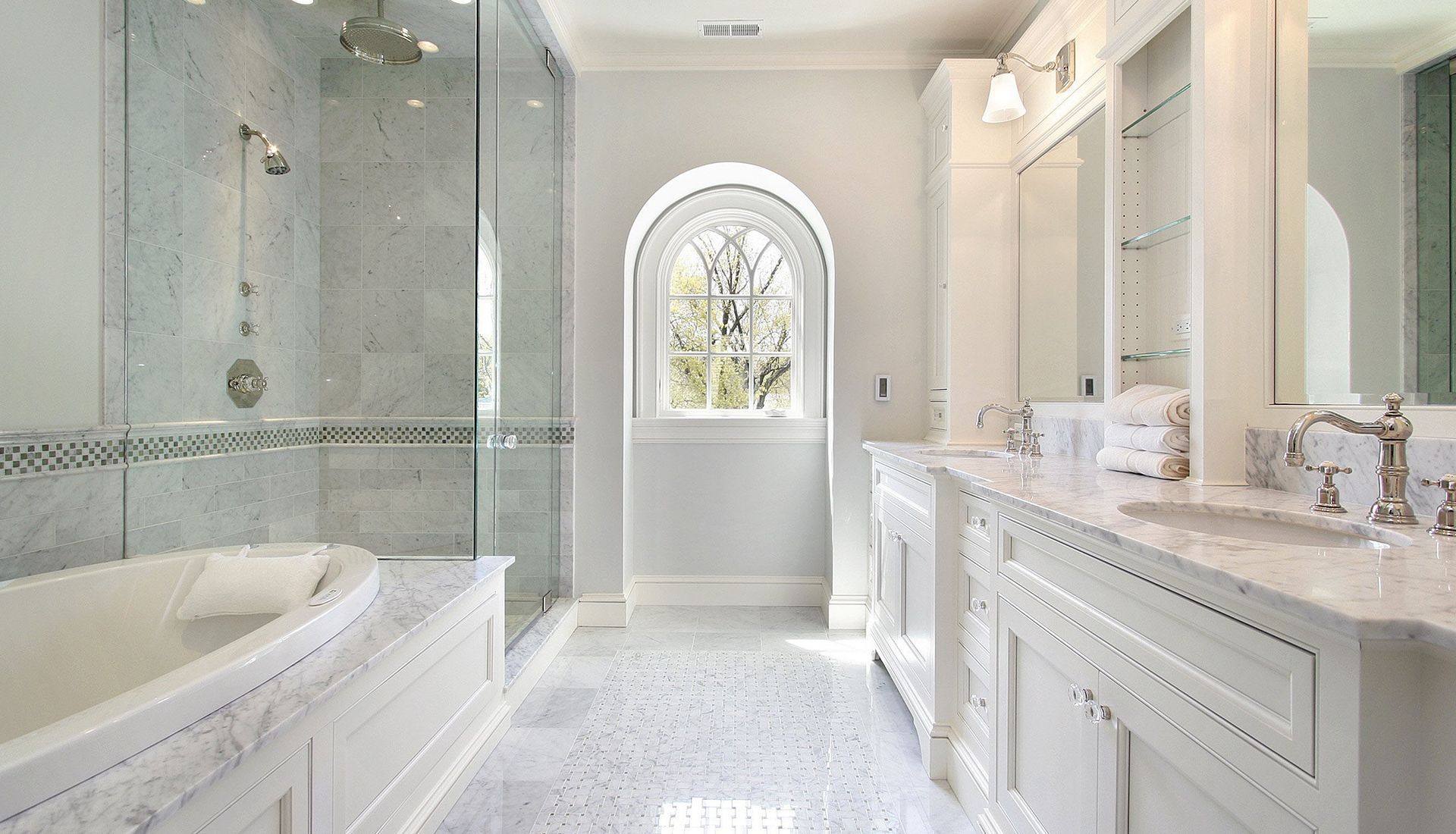 Bright white luxury bathroom with a soaking tub, glass shower, vanity, and arched window.