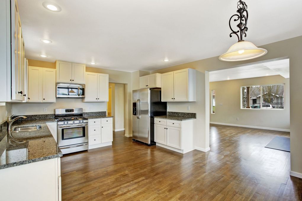 Spacious kitchen with white cabinets, stainless stove and fridge, granite counters, and hardwood floors opening to a dining area