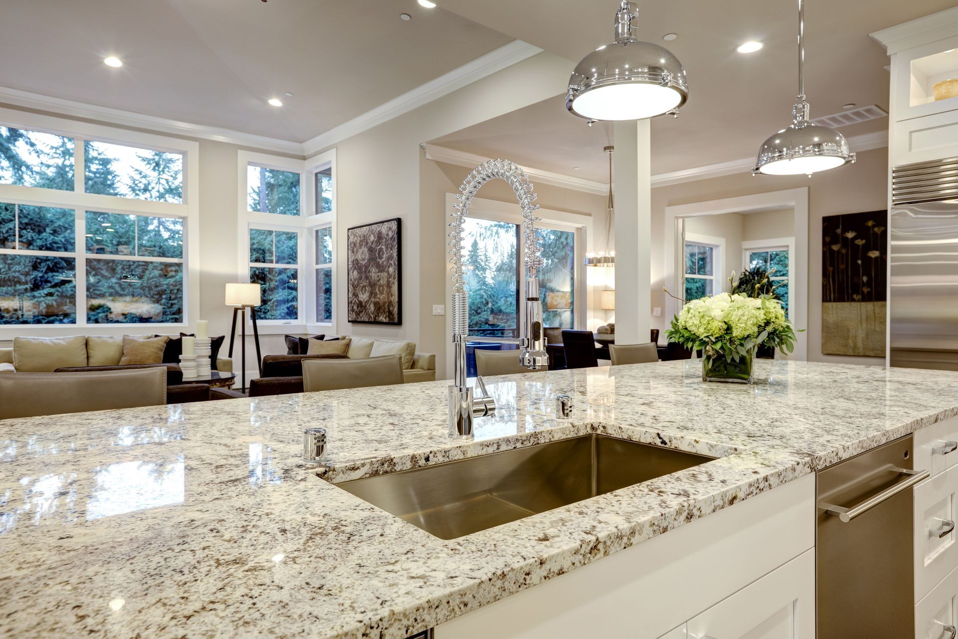 Bright modern kitchen with granite island, pendant lights, and open view to a sunlit living room
