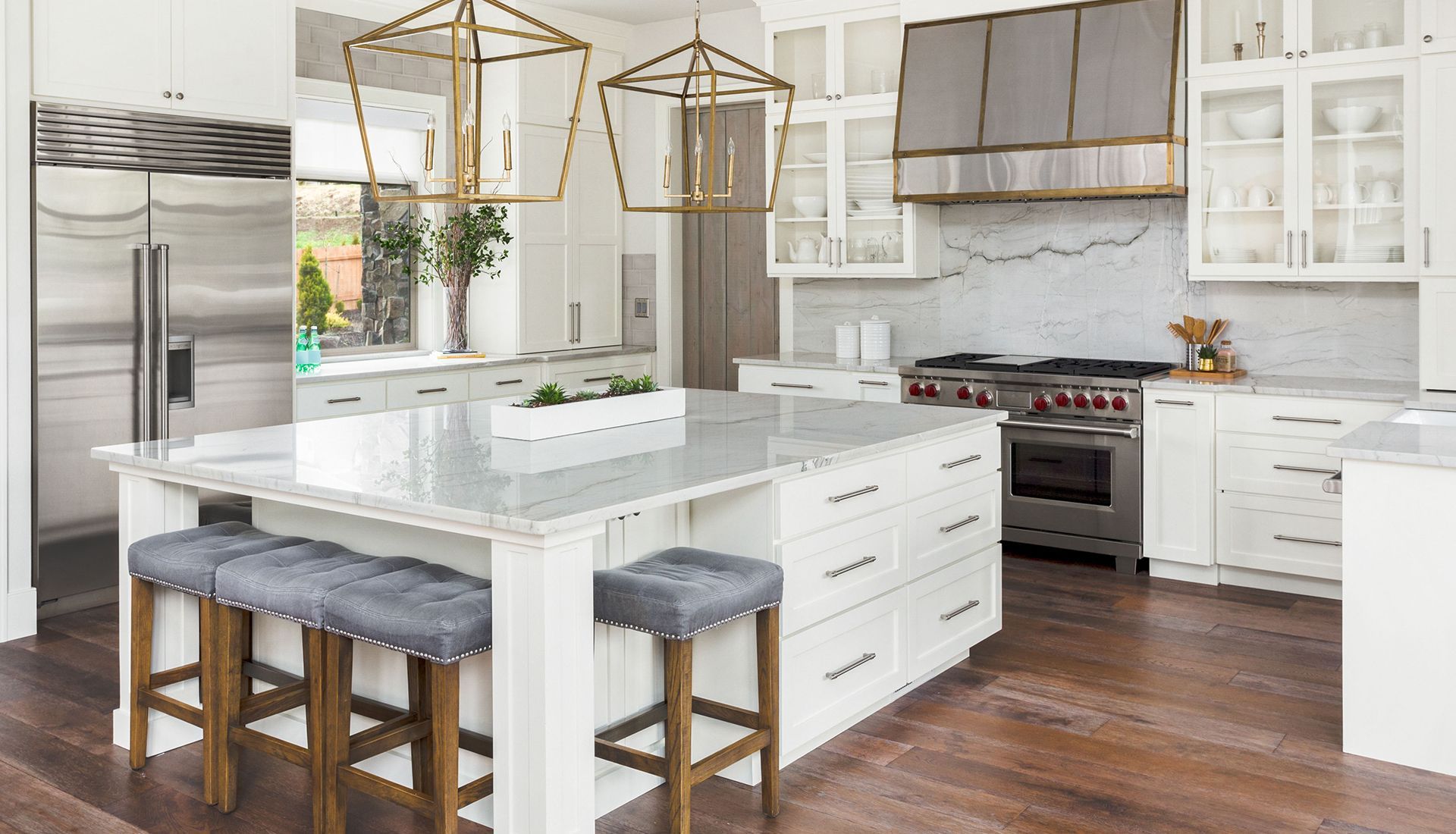Bright modern kitchen with white cabinets, marble island, bar stools, and gold pendant lights