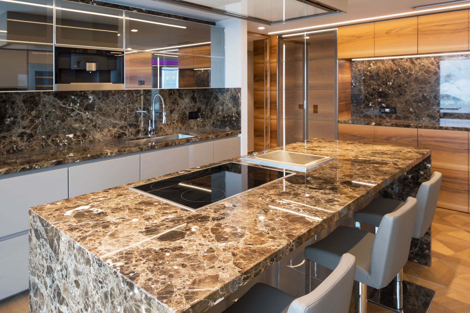 Modern kitchen with brown marble island, built-in cooktop, and bar stools, viewed through reflective glass panels