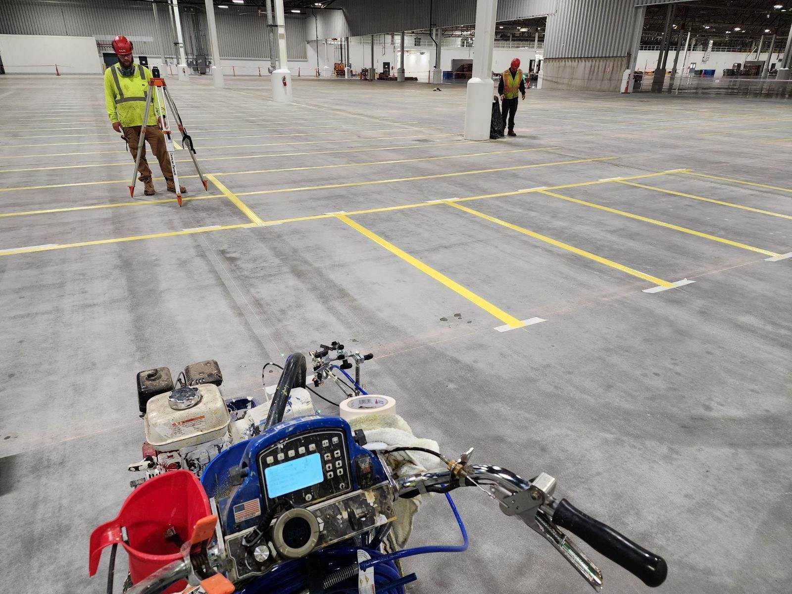 A machine is sitting in a parking lot next to a man painting yellow lines.