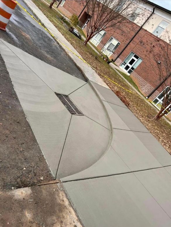 a sidewalk with a drain on the side of it and a brick building in the background