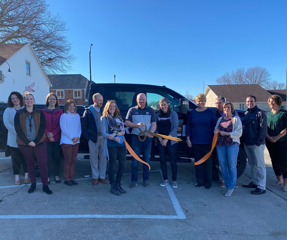 A group of people are standing in front of a van cutting a ribbon.