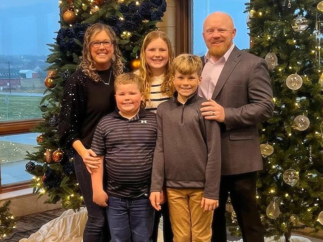 A family is posing for a picture in front of a Christmas tree.