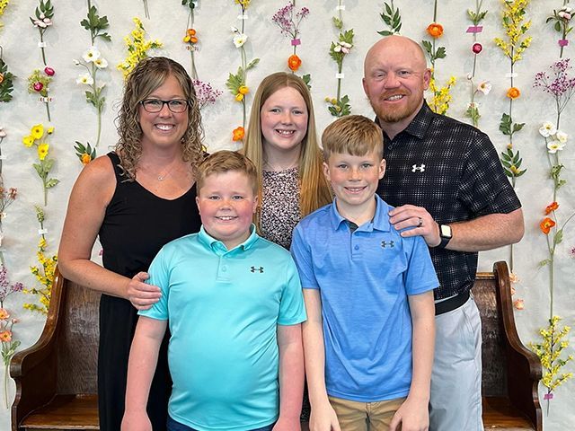 A family is posing for a picture in front of a wall of flowers.