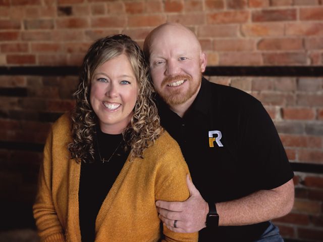 A man and a woman are posing for a picture in front of a brick wall.