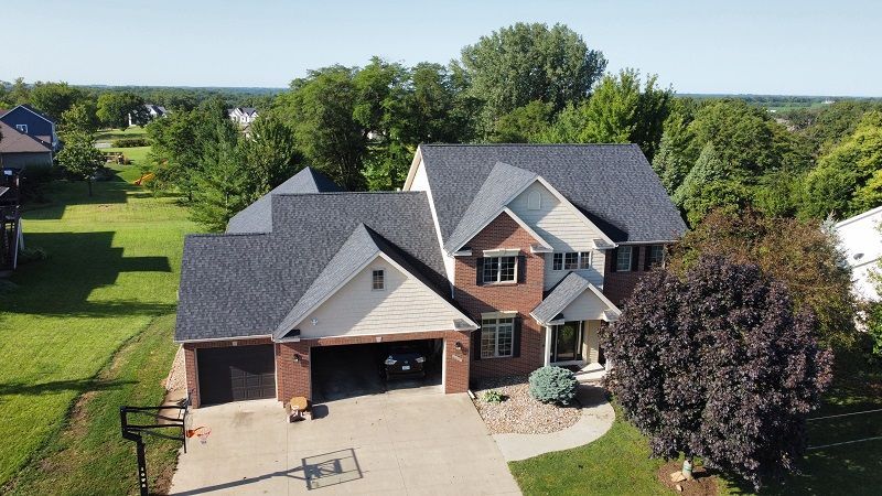 An aerial view of a large brick house with a black roof surrounded by trees.