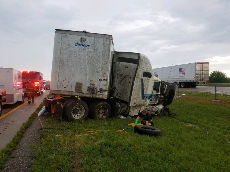Damaged semi-truck off road with emergency vehicles present. The truck is white, on grass.