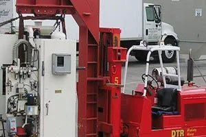 Red industrial machinery next to a white truck; outdoor setting.