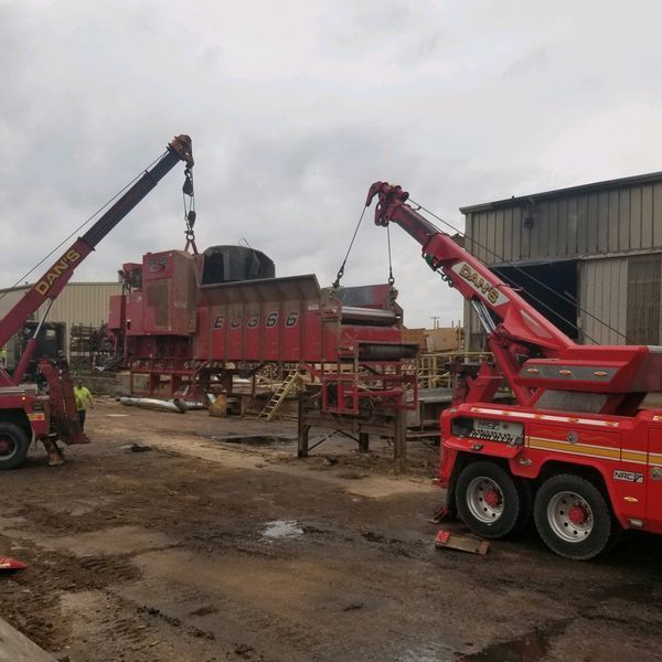 Two red tow trucks lifting a large red industrial machine outdoors.