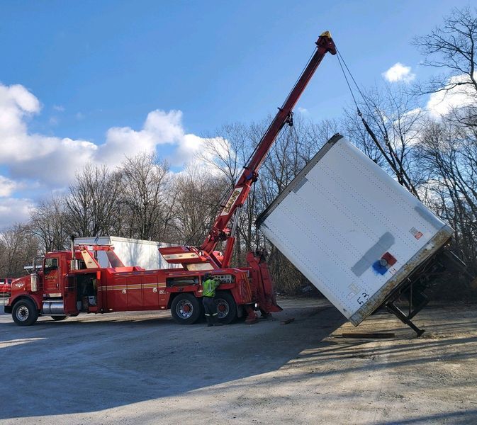 Red tow truck lifting a white cargo container at a parking lot.