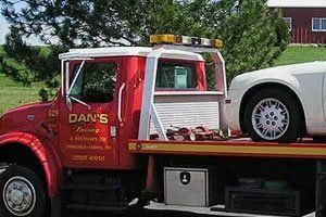 Red tow truck towing a white car on a sunny day. 