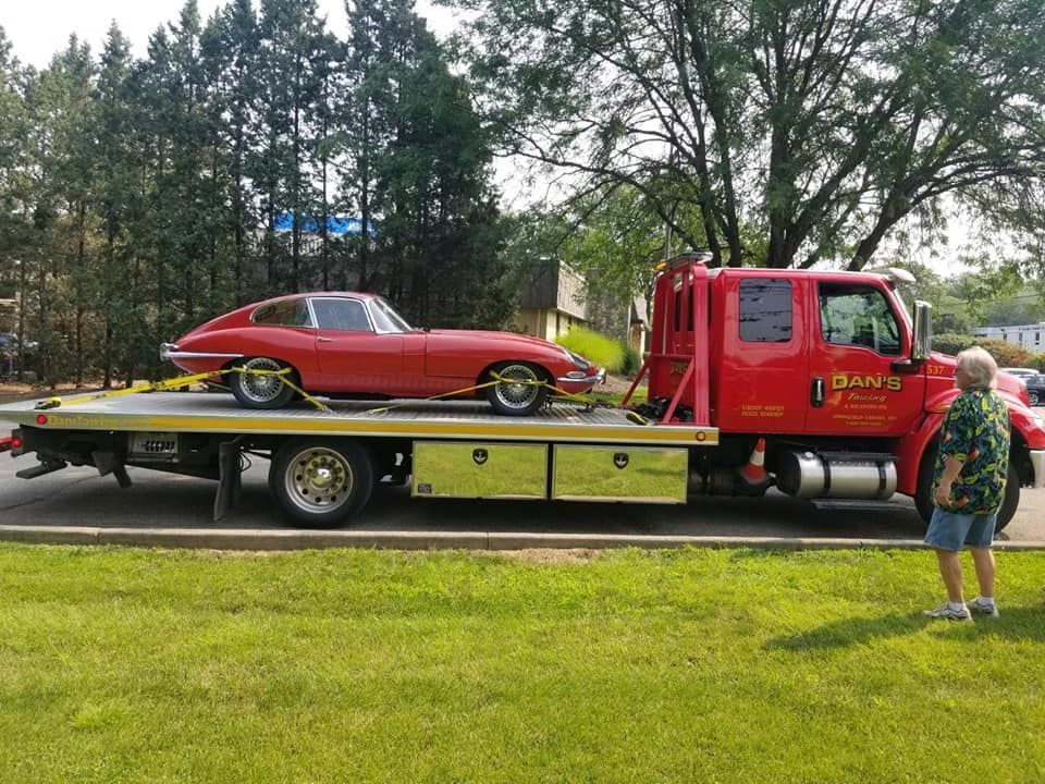 Red Jaguar sports car on a red tow truck, man observing on the grass.