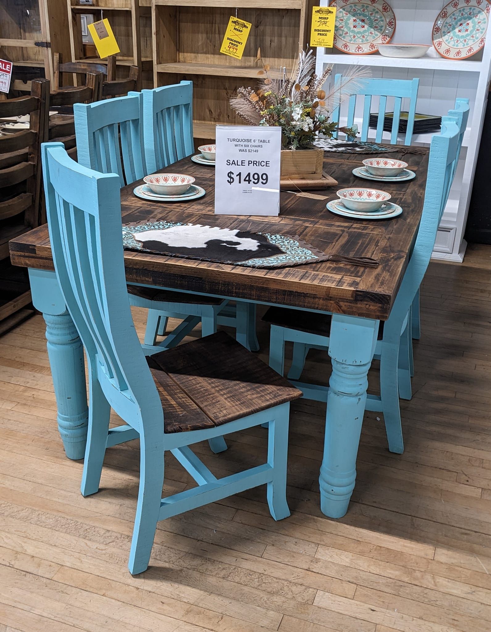 Blue-painted dining table and chairs with rustic wooden tabletop, set in a shop; table is set with plates and flowers.