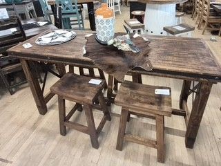 Rustic wooden dining table with two stools and a centerpiece bowl in a furniture showroom