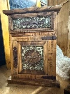Rustic wooden cabinet with carved door, metal hinge, and decorative floral panels