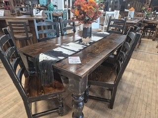 Rustic wooden dining table with black chairs and a flower centerpiece in a restaurant setting