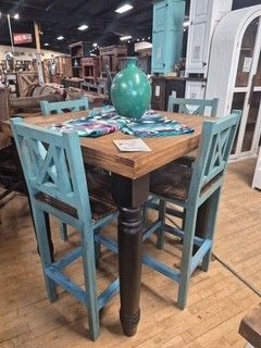 Turquoise bar table with teal chairs and a vase on top in a rustic furniture showroom