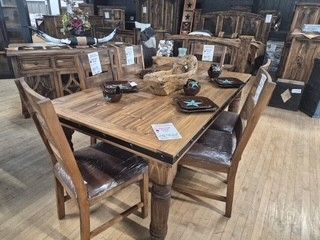 Wooden dining table and four chairs in a furniture showroom, with decor and cabinets in the background