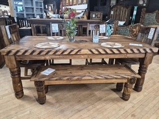 Rustic wooden dining table and bench set with four white plates in a furniture showroom