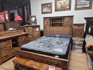 Rustic wooden bedroom set with a black mattress, matching nightstands, red lamp, and framed wall art
