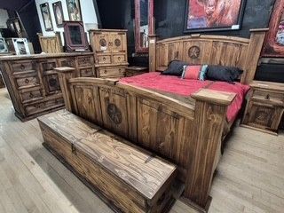 Rustic wooden bedroom set with carved bed, bench, dresser, and red bedding in a showroom