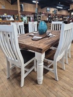 Rustic dining table with white chairs and a blue vase in a furniture showroom