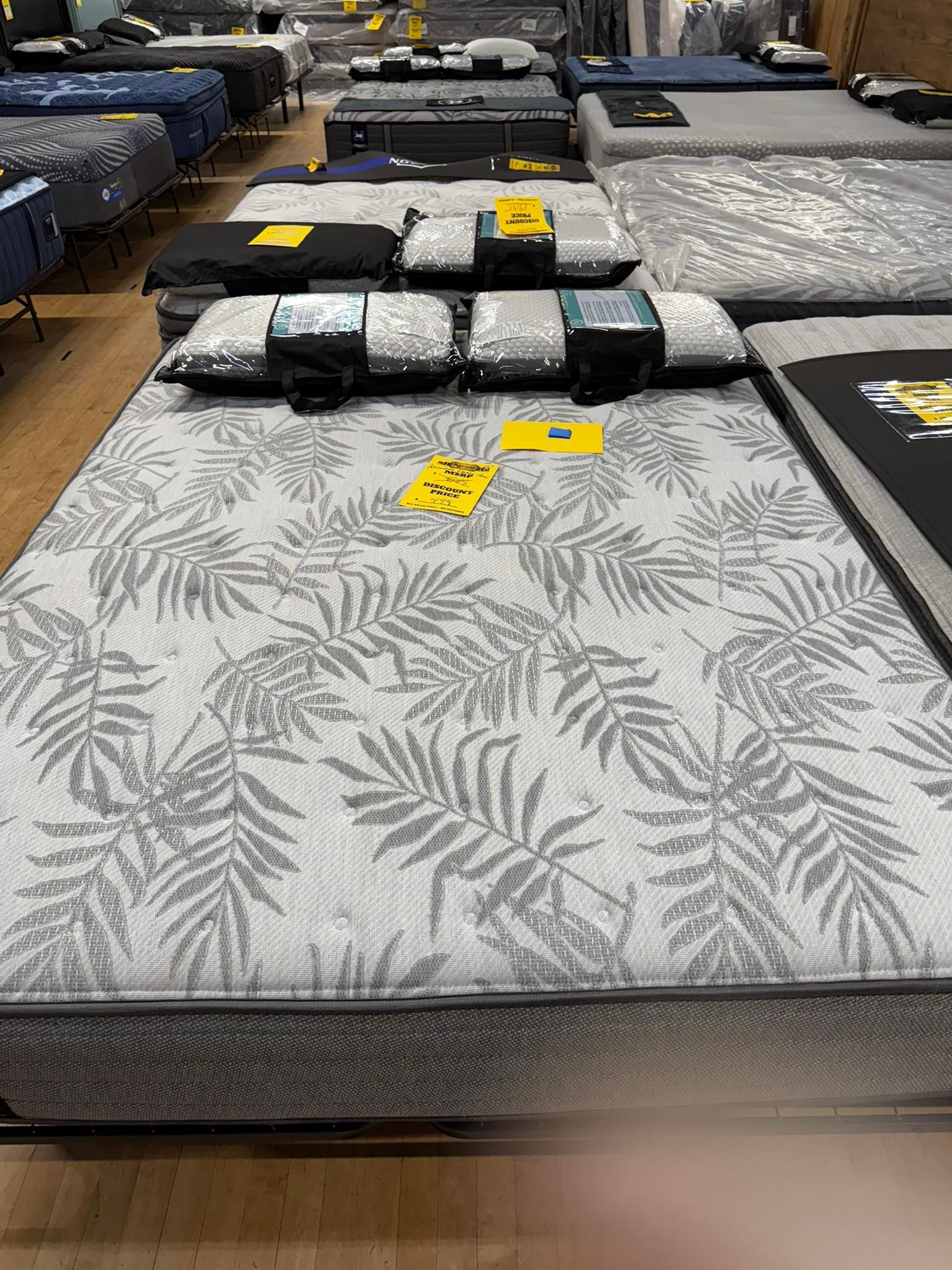 Mattresses on display in a store, arranged in rows. Gray patterned mattress in foreground.