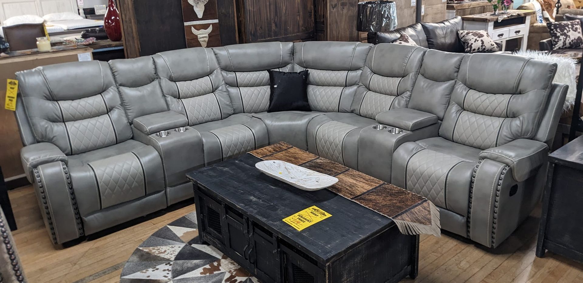 Gray sectional sofa with recliner seats, a black pillow, and a dark coffee table in a showroom.