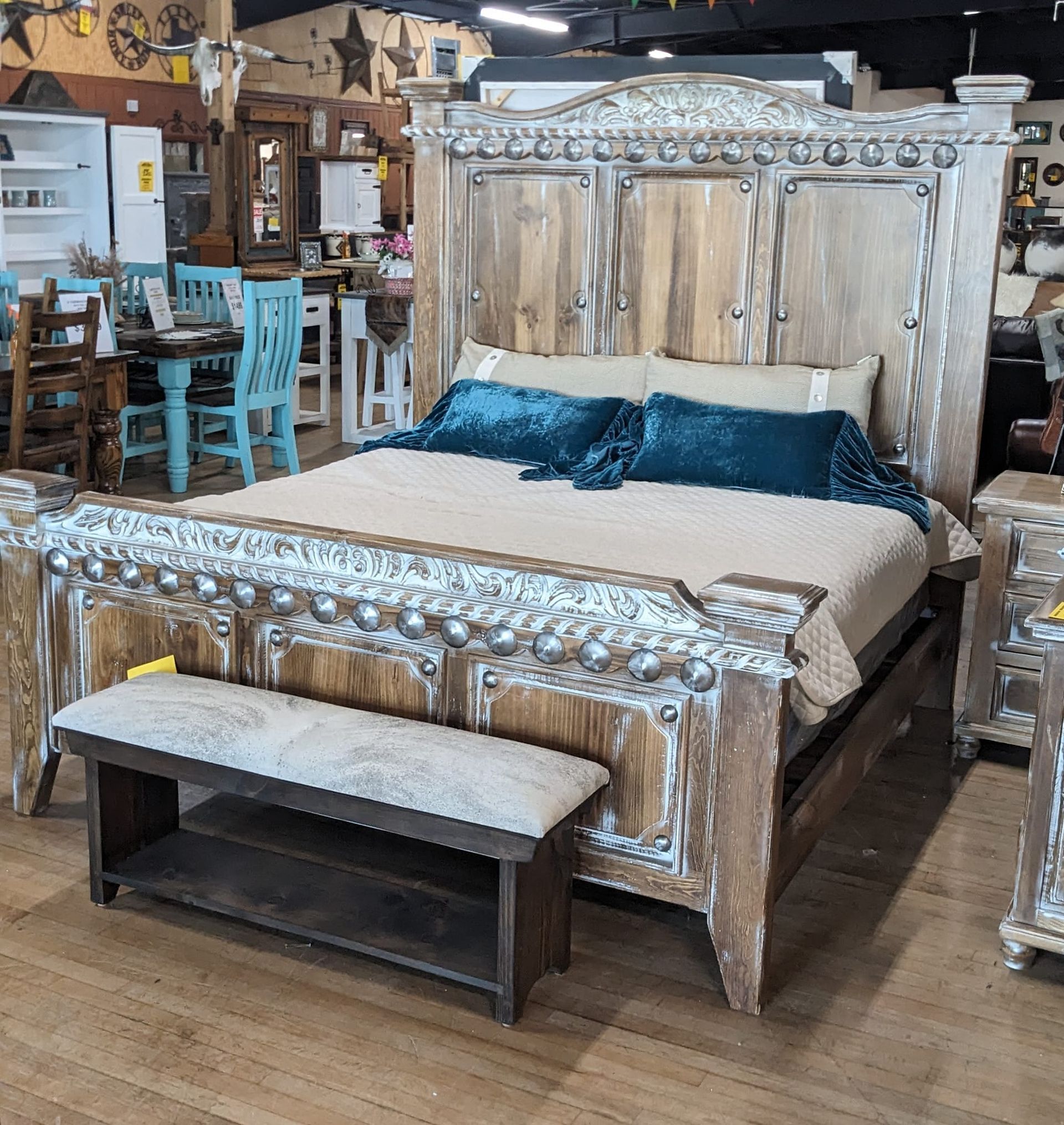 Rustic wooden bed with teal pillows and a bench in a furniture store.