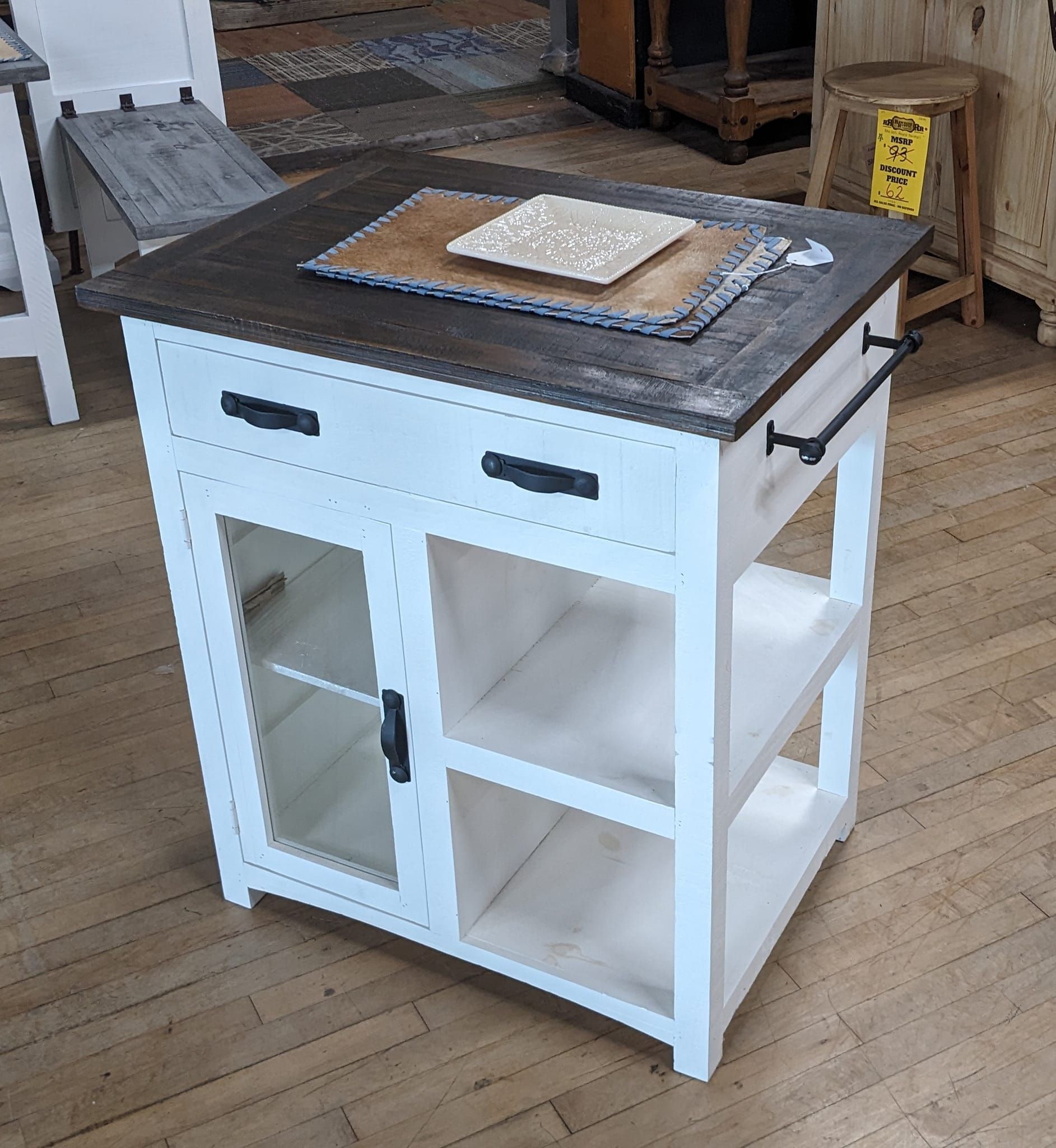 White kitchen island with a dark wood top and glass-doored cabinet, two shelves, and a drawer.