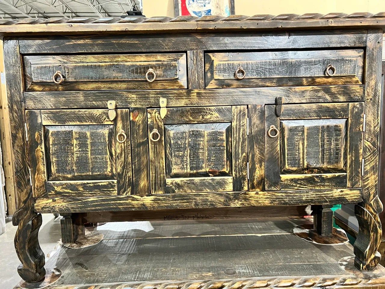 Rustic, dark wooden cabinet with drawers and doors, distressed finish, ornate legs.