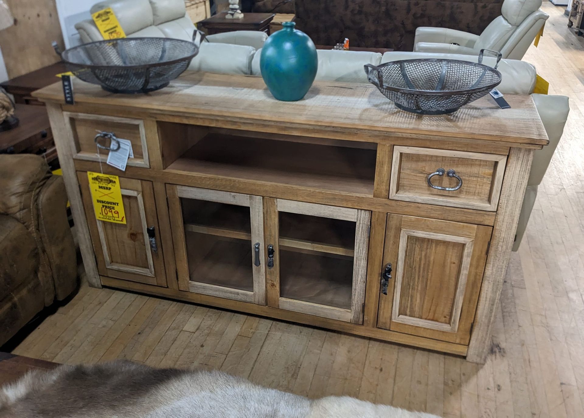 Wooden entertainment center with storage drawers and glass-front doors, set in a store.