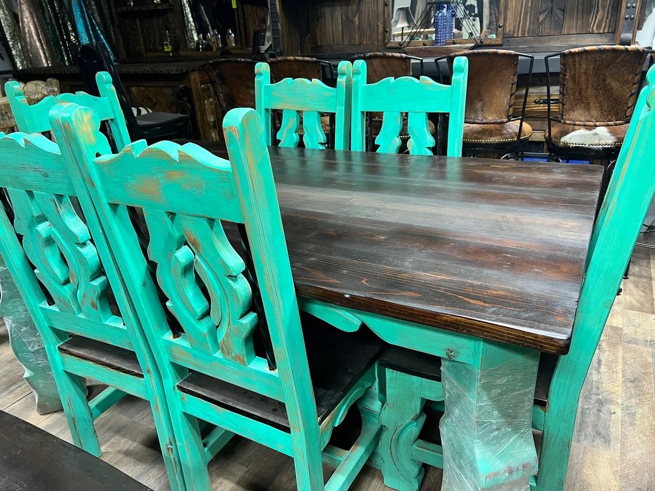Turquoise dining set: wooden table, chairs with ornate backs, in a rustic setting.