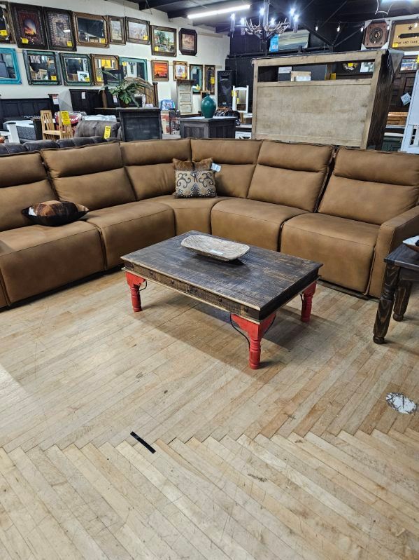 Brown sectional sofa with a rustic coffee table and red legs in a showroom.
