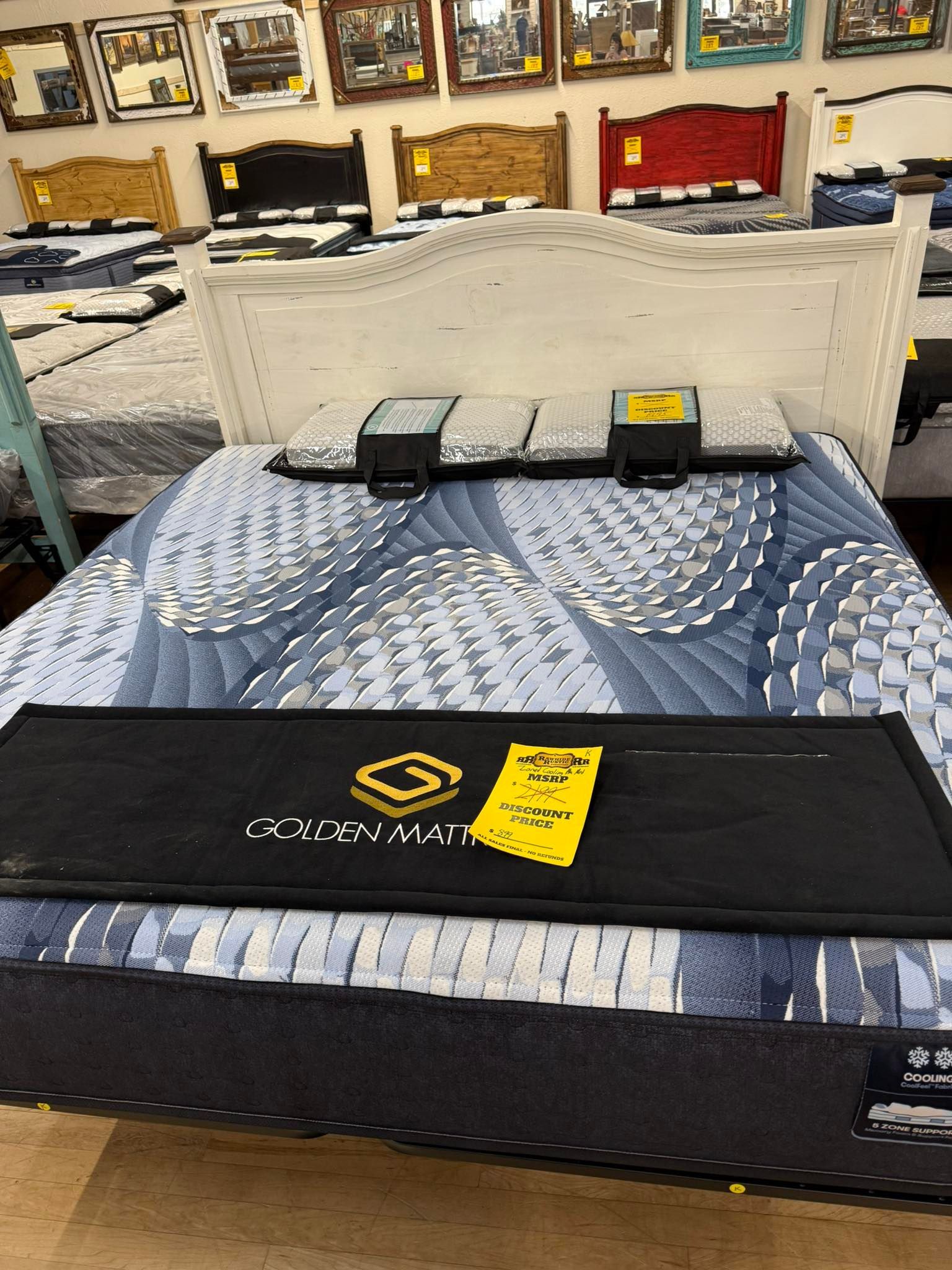 Bed with blue patterned mattress, white headboard, and price tags in a furniture store.