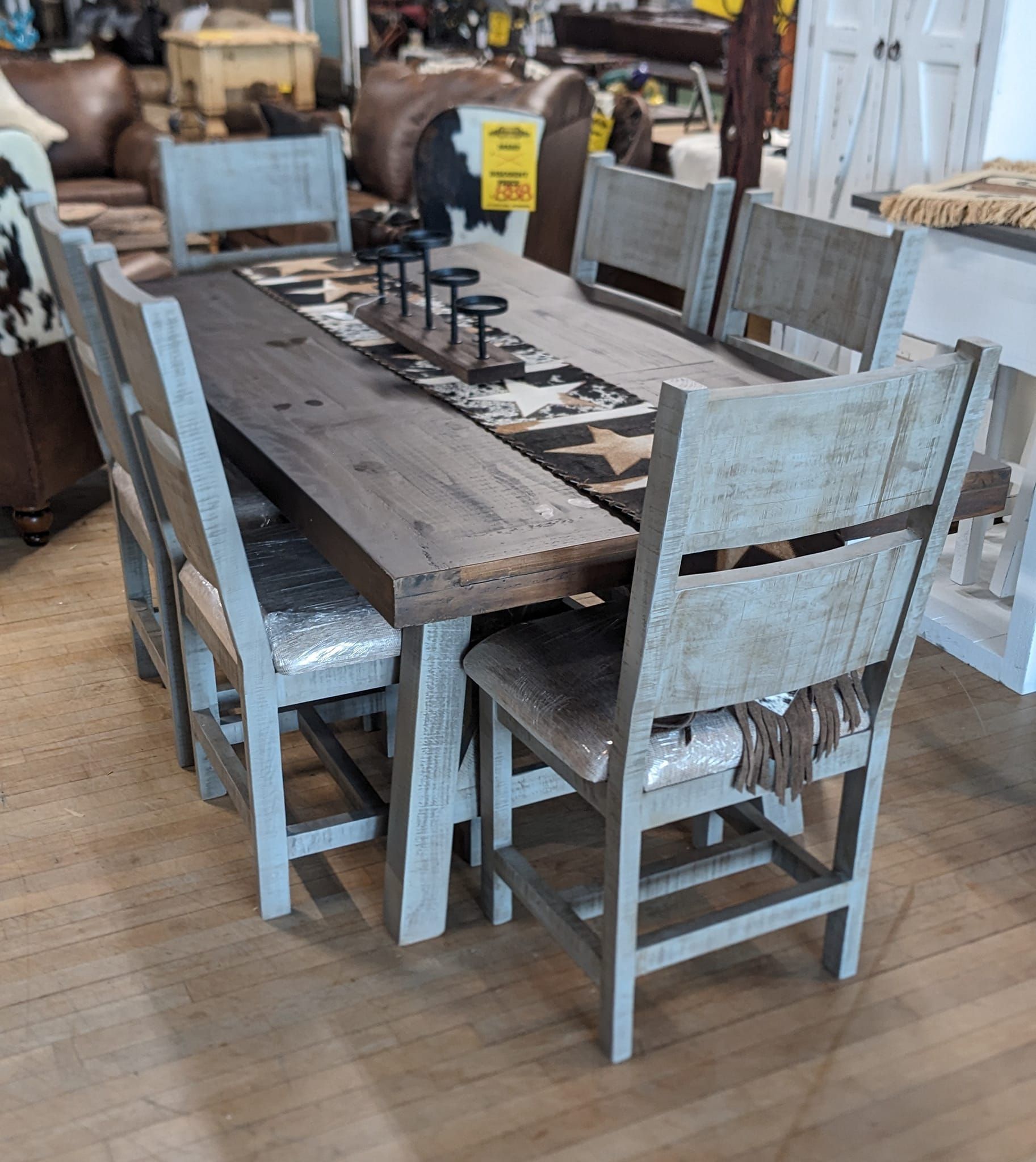 Rustic wooden dining table with six matching chairs, candles, and cowhide runner in a furniture store.