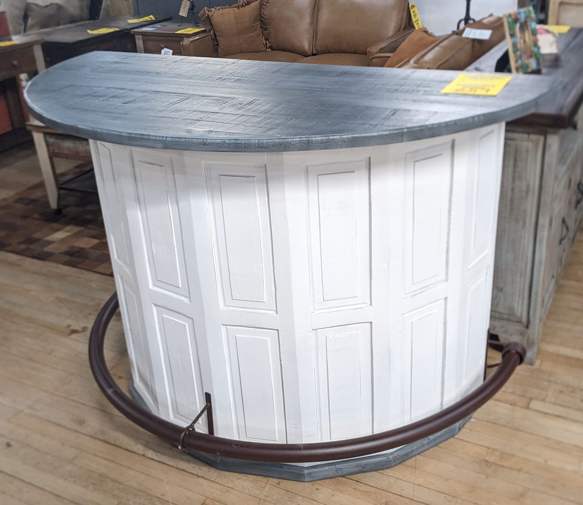 White and gray rustic bar with a curved top and footrest, set in a furniture store.