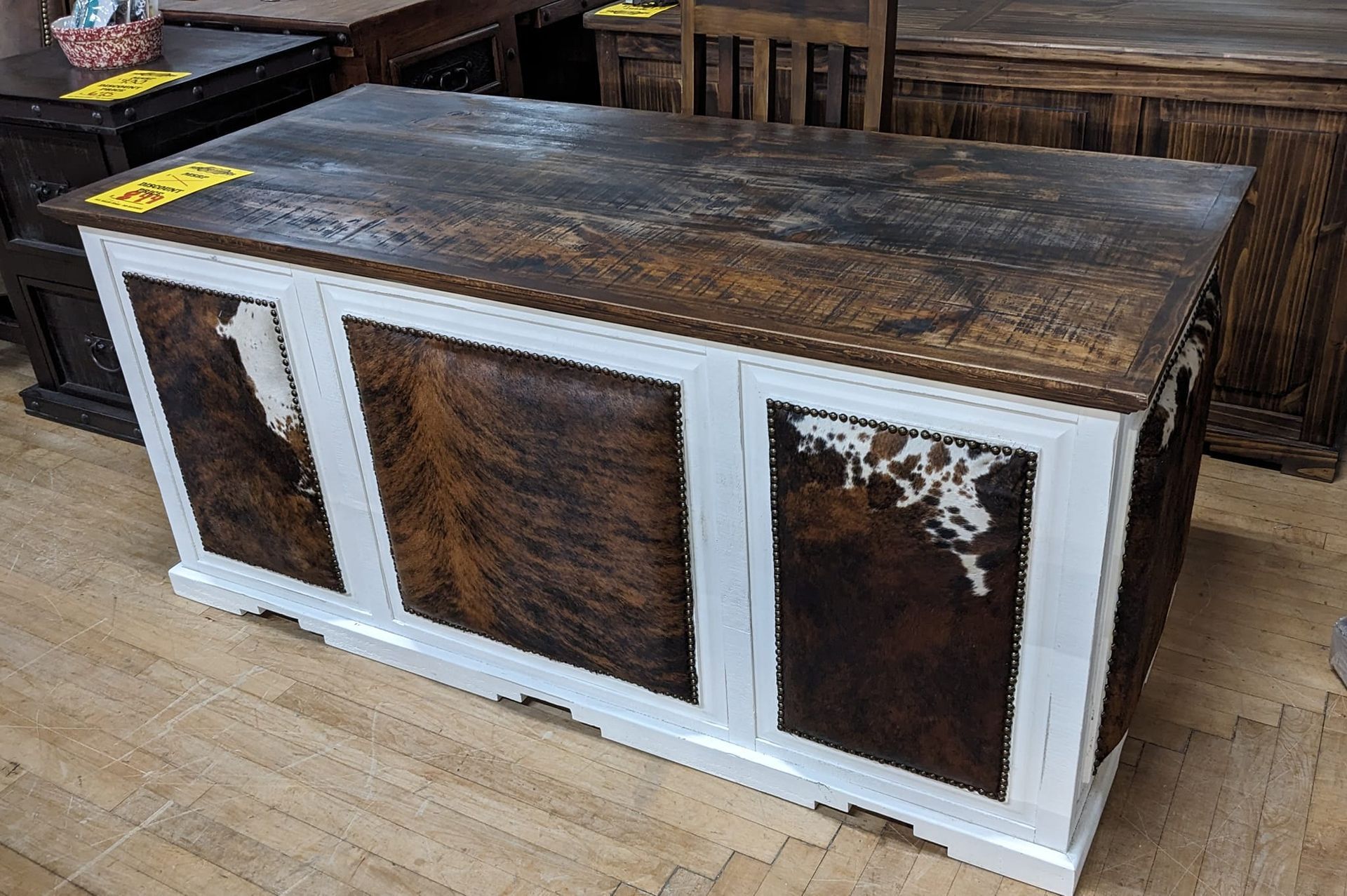 Wooden desk with white trim, cowhide panels, and dark wood top, in a store.