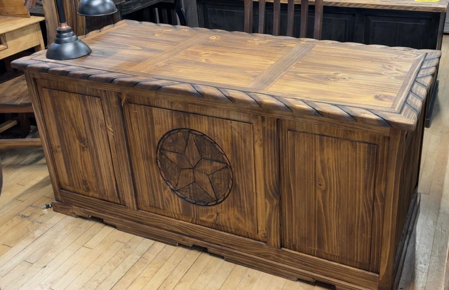 Wooden desk with carved star on the front, rope trim, in a room with wood floors.