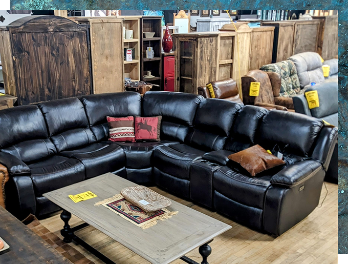 Black leather sectional sofa in a furniture store, with a coffee table in front.