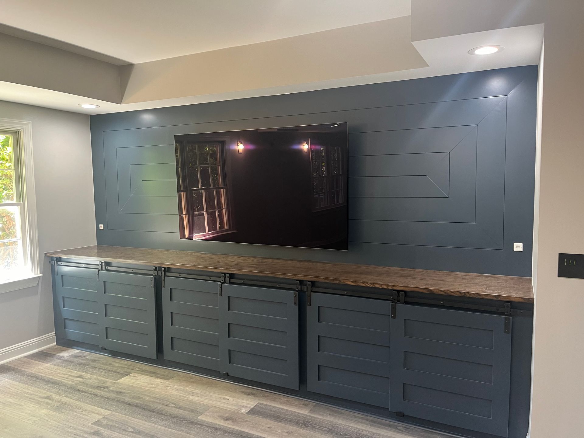 A mounted TV on a navy blue accent wall above a cabinet with matching navy cabinets in a room.