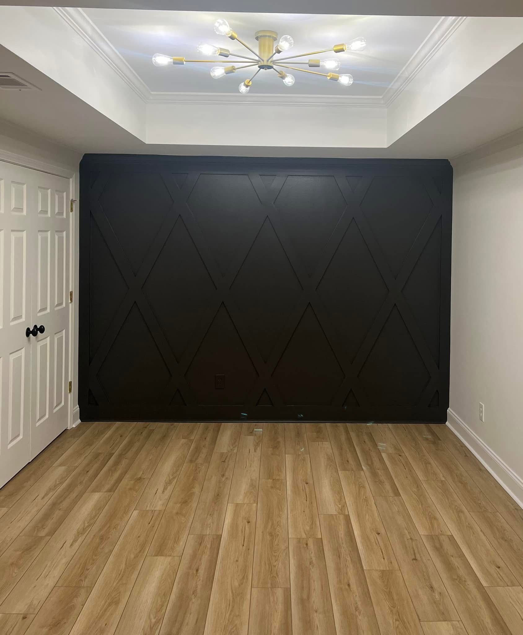 Room with wood-look flooring, white walls, black diamond-patterned accent wall, white ceiling, and a chandelier.