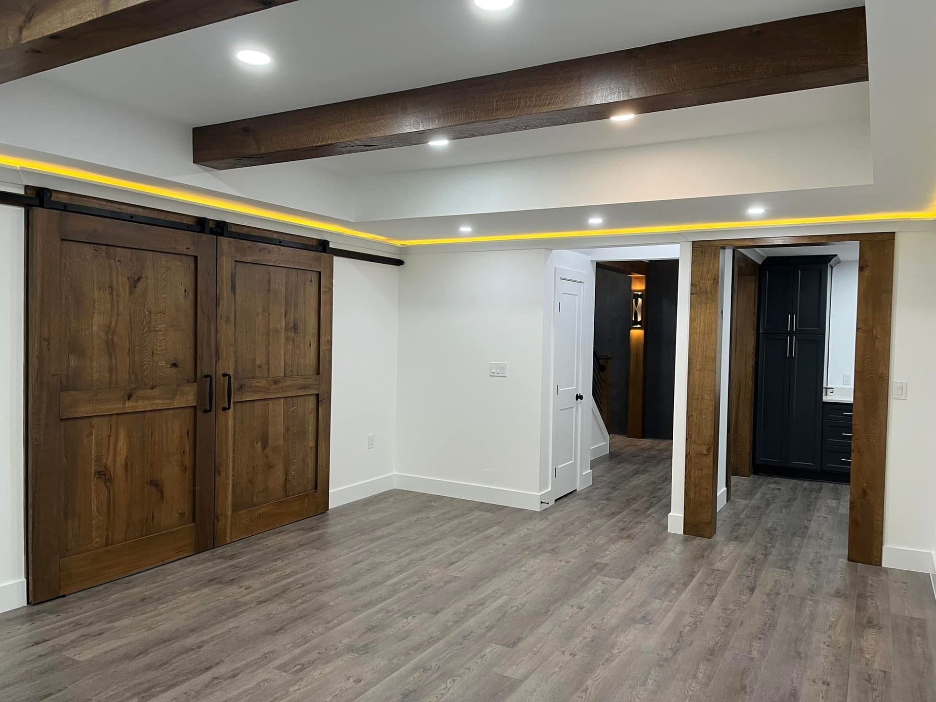 Spacious room with wood-paneled sliding doors, wooden beams, recessed lighting, and grey flooring.