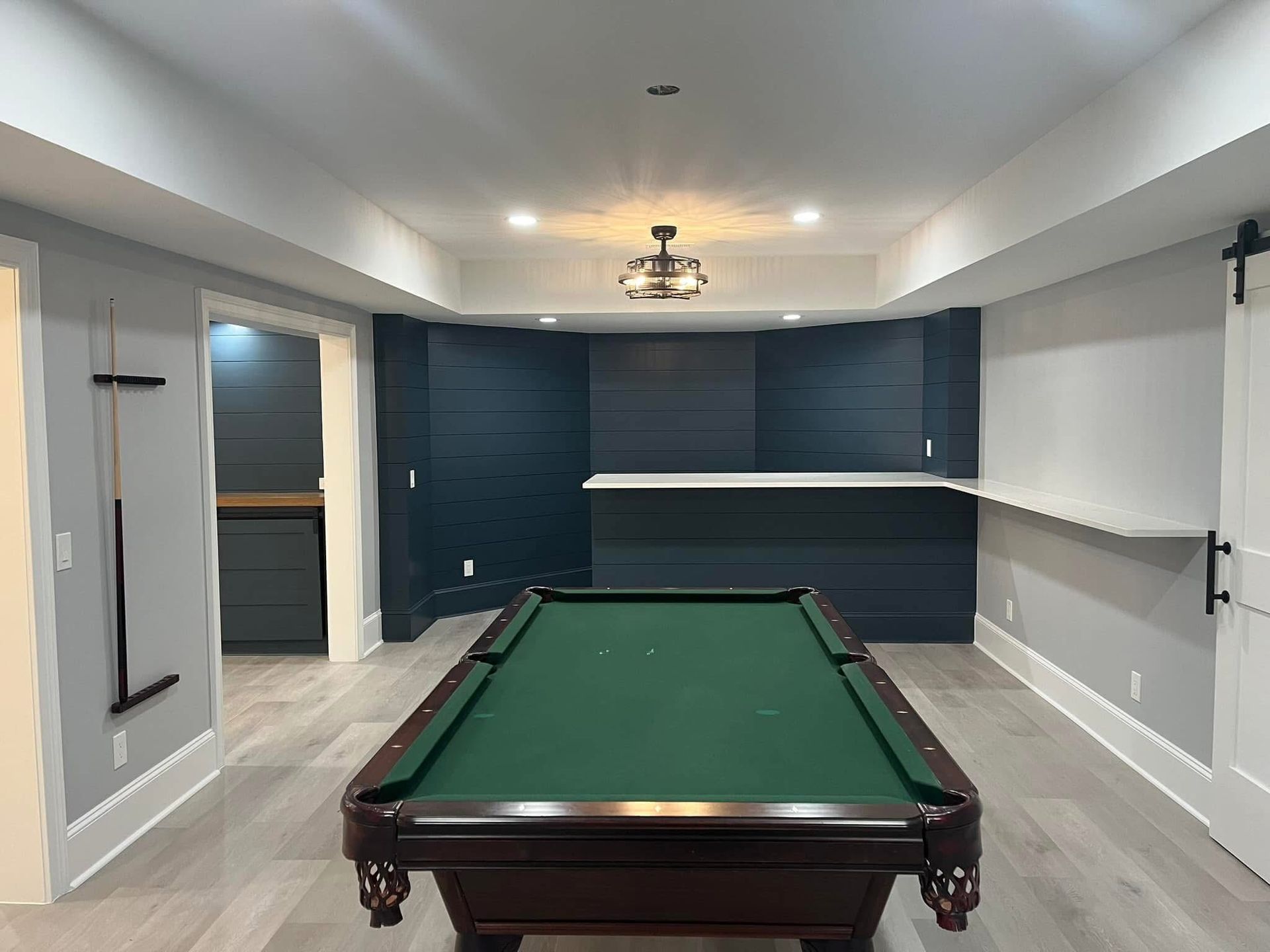 Pool table in a finished basement with a bar, wood paneling, and a sliding barn door.