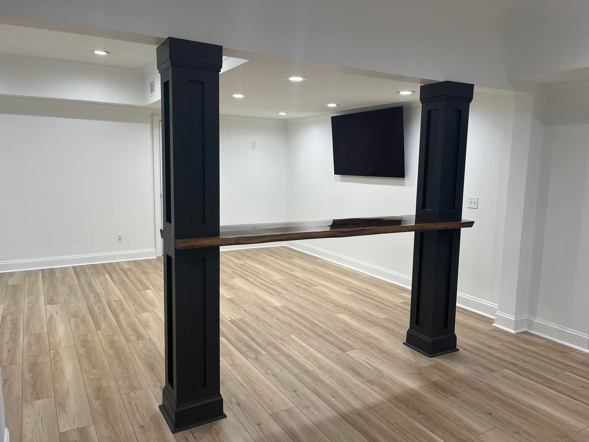 Basement room with black pillars, a wooden bar, and a mounted TV.