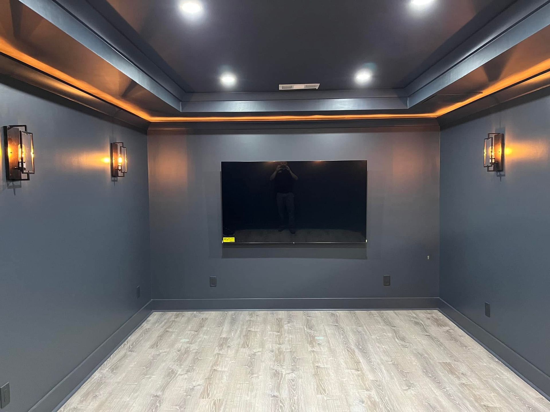 Dark blue media room with a large TV, sconces, and LED lighting in the ceiling.