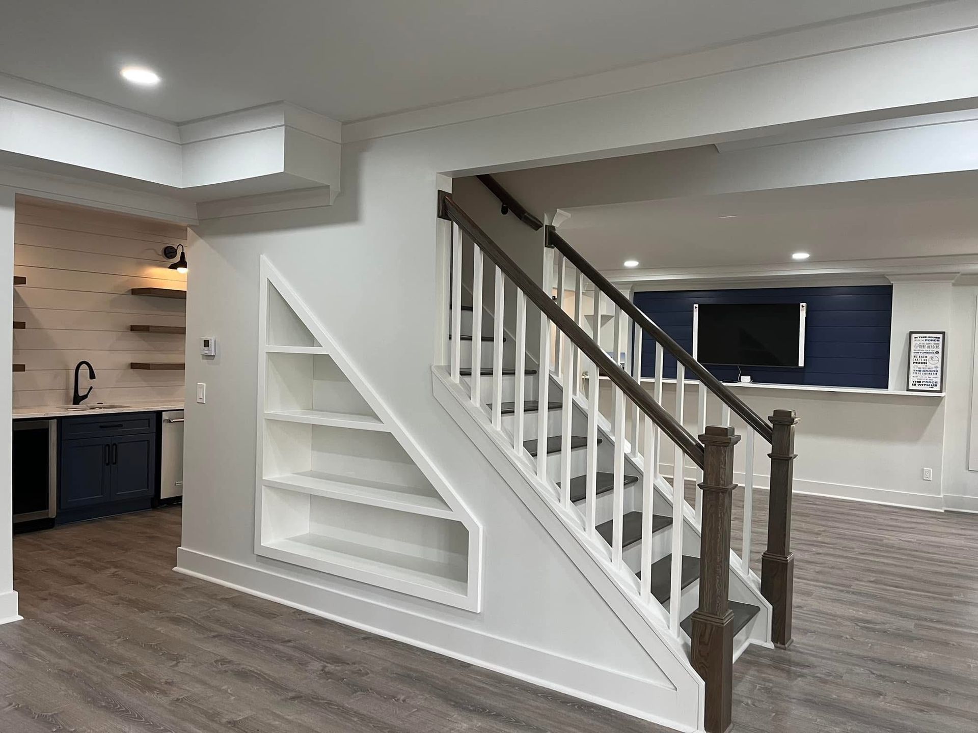Interior view of a finished basement with a staircase, built-in shelves, and a bar area with a TV.